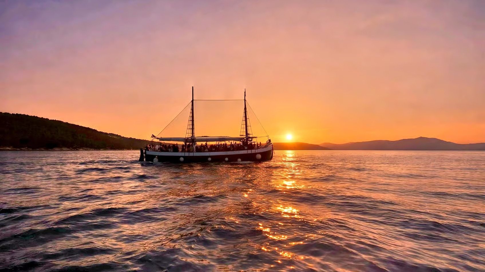 Antique wooden boat with guests cruising at golden hour near Split